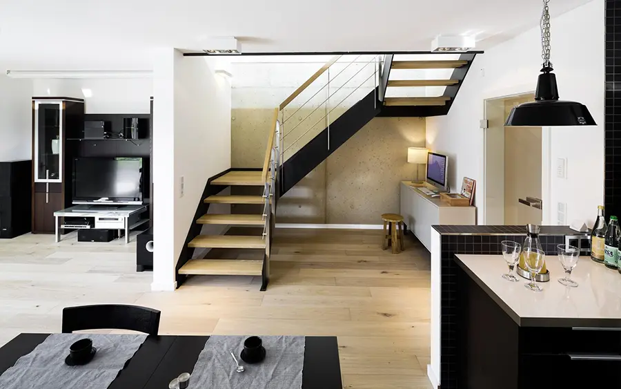 Moderne Küche und Essbereich mit Holzböden, einem Groneck-Esstisch für zwei Personen, schwarzen Pendelleuchten und einer offenen Treppe mit Metallgeländer.