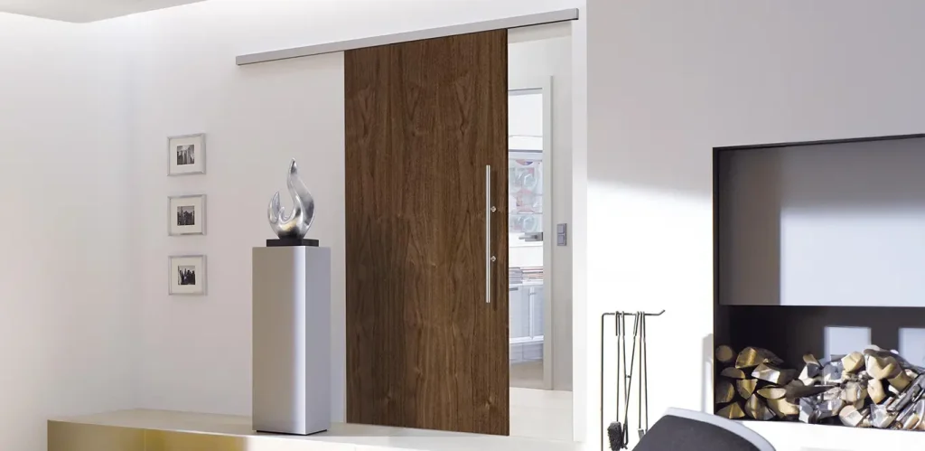 Ein modernes Wohnzimmer mit Schiebetüren, einer eleganten weißen Konsole mit einer dekorativen Skulptur, einem montierten Flachbildfernseher und einem mit Holzscheiten gefüllten Kamin auf der rechten Seite.