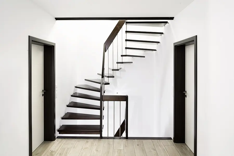 Eine moderne freitragende Treppe mit dunklen Stufen kontrastiert mit weißen Wänden in einem minimalistischen Innenraum, flankiert von geschlossenen Türen.
