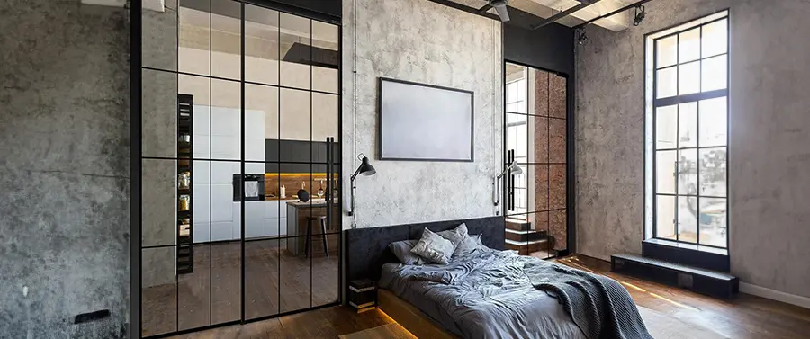 Ein modernes Schlafzimmer im Industriedesign mit Betonwänden, schwarz gerahmter Glastrennwand mit eleganten Türgriffen und großen Fenstern für viel Tageslicht.