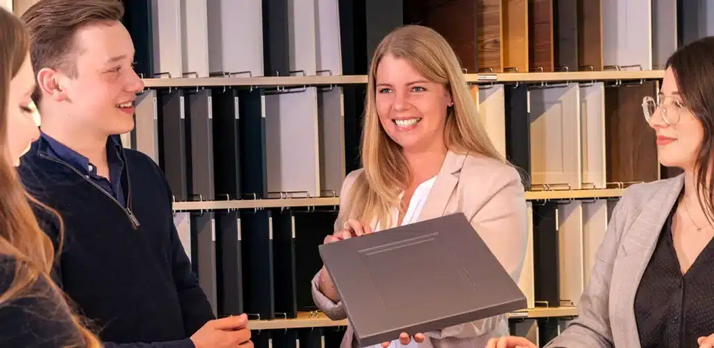 Eine Gruppe junger Berufstätiger in einem Häcker-Unternehmen, wobei eine Frau ein Dokument oder eine Mappe in der Hand hält und ihren Kollegen präsentiert.