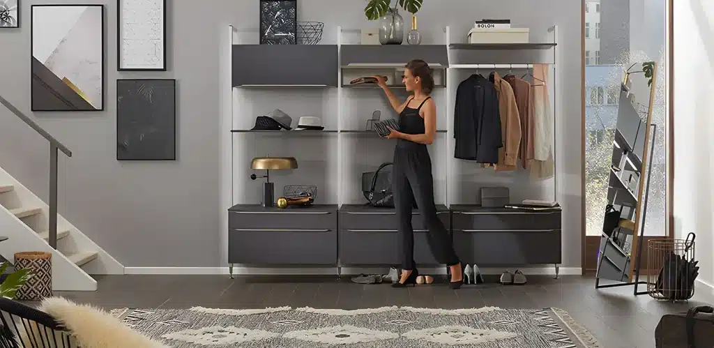 Eine Frau in lässigem Outfit ordnet Gegenstände auf einem modernen Aufbewahrungsmöbel in einer gut beleuchteten, hübsch dekorierten Wohnzimmereinrichtung mit einer Treppe im Hintergrund.
