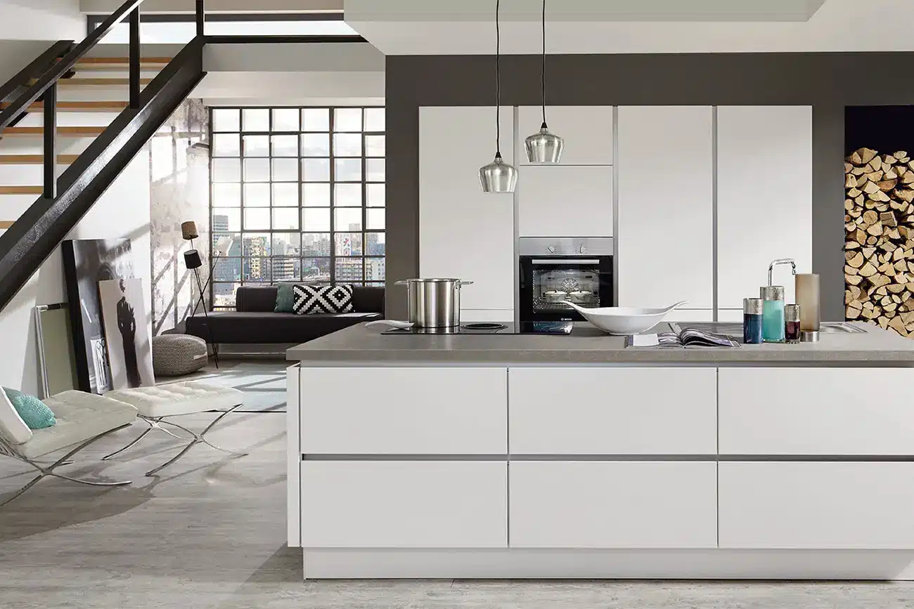 Moderne Küchen mit klaren Linien, weißen Schränken und einer zentralen Kücheninsel vor dem Hintergrund eines Wohnbereichs mit einer Treppe im Loft-Stil.