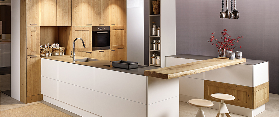 Moderne Küche mit hellen Holzschränken und weißen Arbeitsplatten, darunter eine zentrale Insel und Pendelleuchten.
