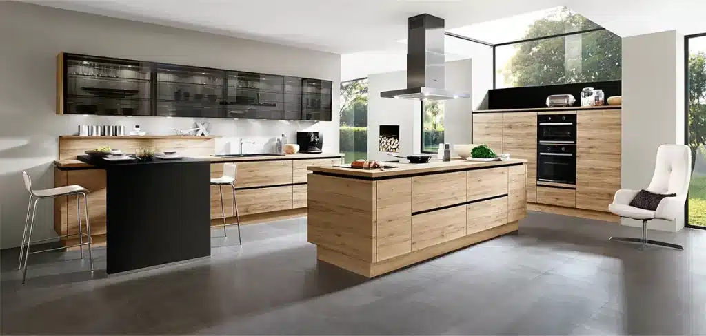 Eine moderne Küche mit eleganten schwarzen Geräten, hellen Holzschränken, einer zentralen Insel und einem Essbereich von Natural Living Küchen mit weißem Stuhl und Tisch.