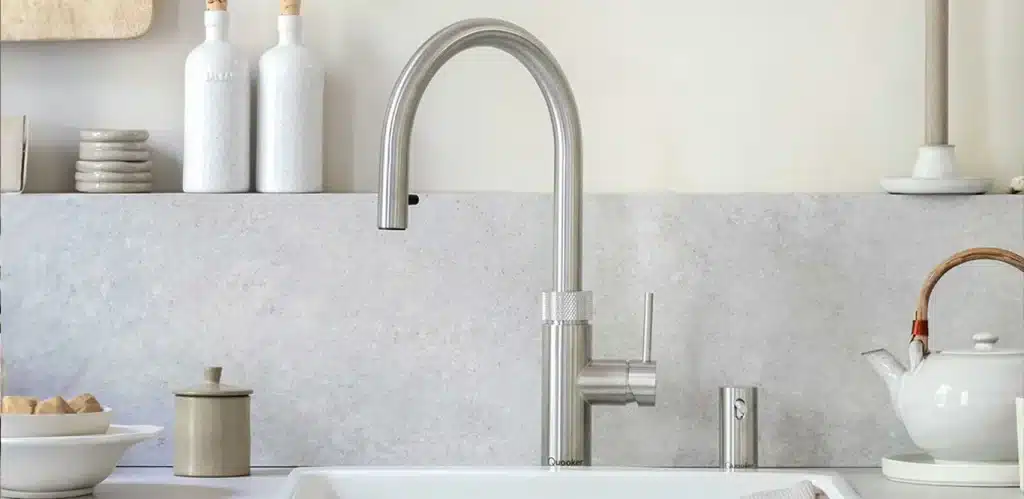 Modernes Küchenspülbecken mit Quooker-Wasserhahn, umgeben von Accessoires und Küchenutensilien in neutralen Farbtönen.