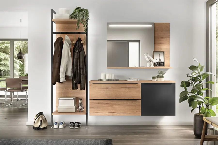 Ein moderner Eingangsbereich mit einer Garderobe mit Jacken, einer Holzbank mit Stauraum, einem Spiegel und einigen dekorativen Pflanzen. Im Hintergrund bieten Regalsysteme zusätzliche Aufbewahrungs- und Organisationsmöglichkeiten.