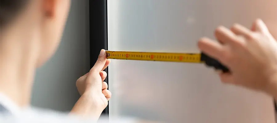 Eine Person misst mit einem Maßband die Breite eines Fensters in Innenräumen.