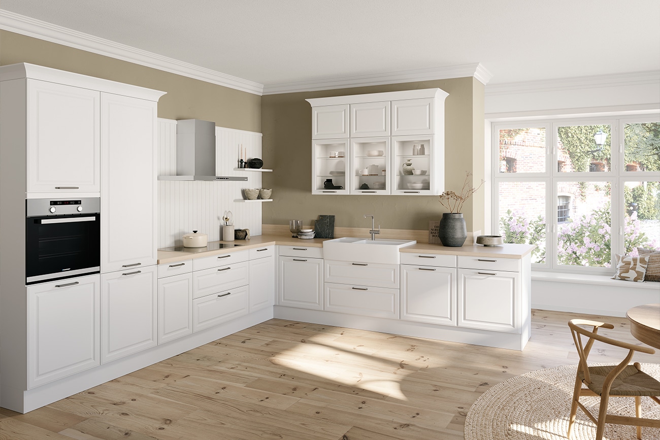 Ein modernes Landhausküchen-Interieur mit weißen Schränken, Holzböden und Blick ins Freie durch die Fenster.